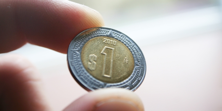 One Mexican peso coin held in someone's hand